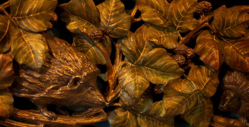 Hérisson à demi caché sous un amas de feuilles sèches, au pied d'une haie