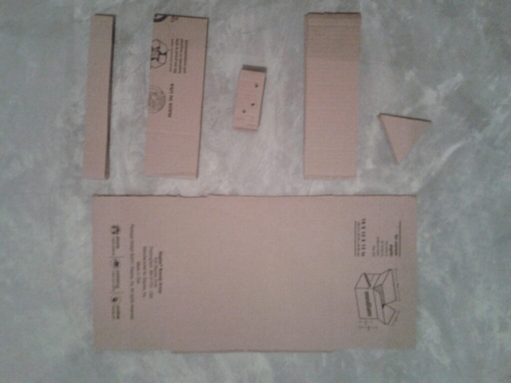 Morceaux de carton brun d&eacute;chir&eacute;s &agrave; la main, empil&eacute;s &agrave; c&ocirc;t&eacute; d'un bac de compostage